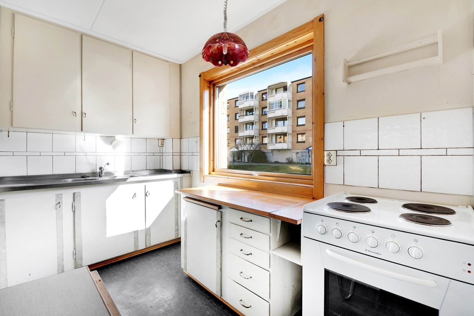 Kjøkken med belegg på gulv, malte vegger og malt tak. Original kjøkkeninnredning med malte slette fronter, heltre benkeplate med fliser over og dobbel oppvaskkum med helt benkebeslag. Komfyr og kjøleskap følger. Galleribilde