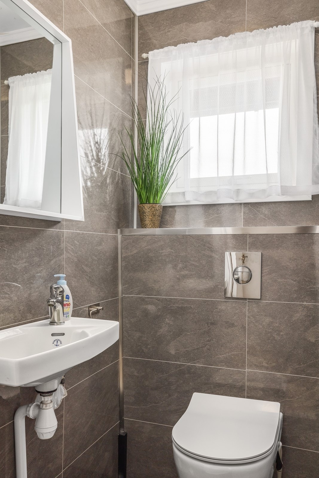 Vegg-i-vegg med bad er det et separat og praktisk toalettrom med veggehengt wc og en liten vask. Toalettrom med baderomsplater på vegger likt som baderom. Galleribilde