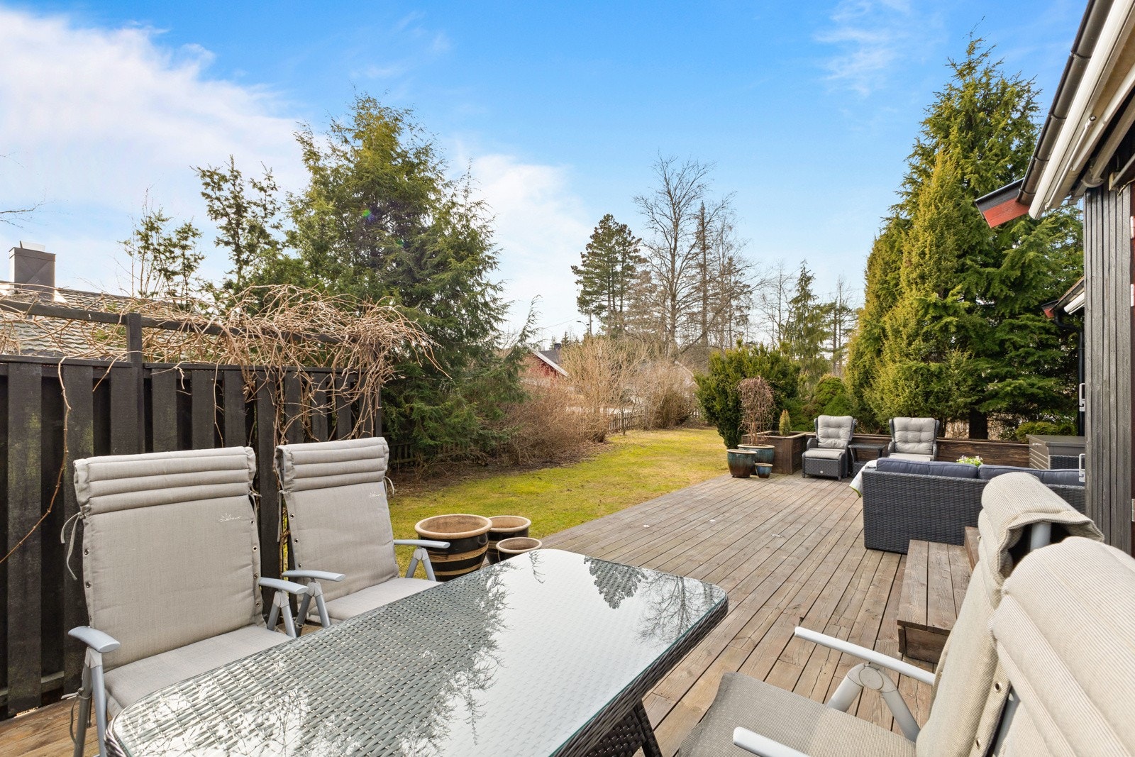 Romslig terrasse med sittegruppe og spisebord. Utsikt mot hage med trær og busker. Galleribilde