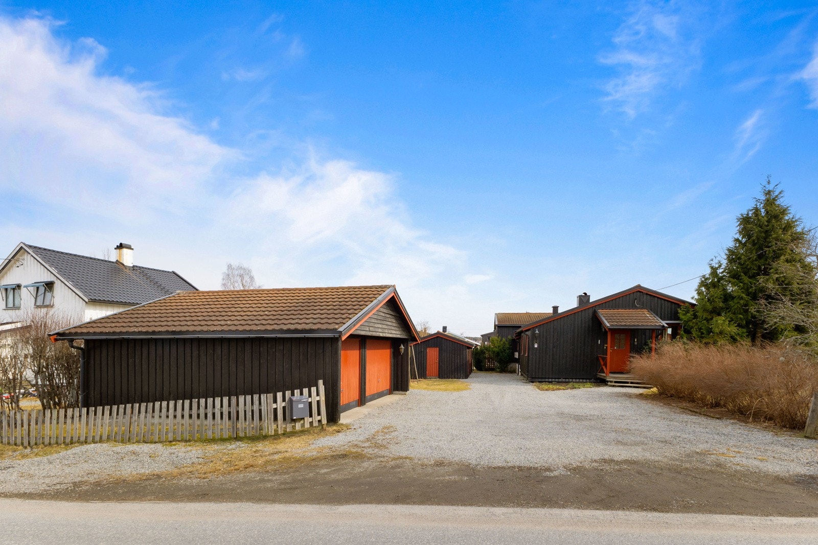 Boligen har svart kledning, røde detaljer og en gruslagt gårdsplass. Garasje med plass til to biler. Galleribilde