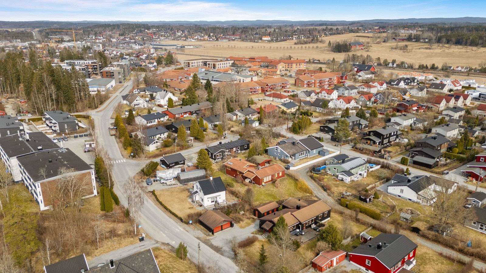 Oversiktsbilde av et boligområde med en blanding av eneboliger og leilighetsbygg, omgitt av skog og åpent landskap. Galleribilde