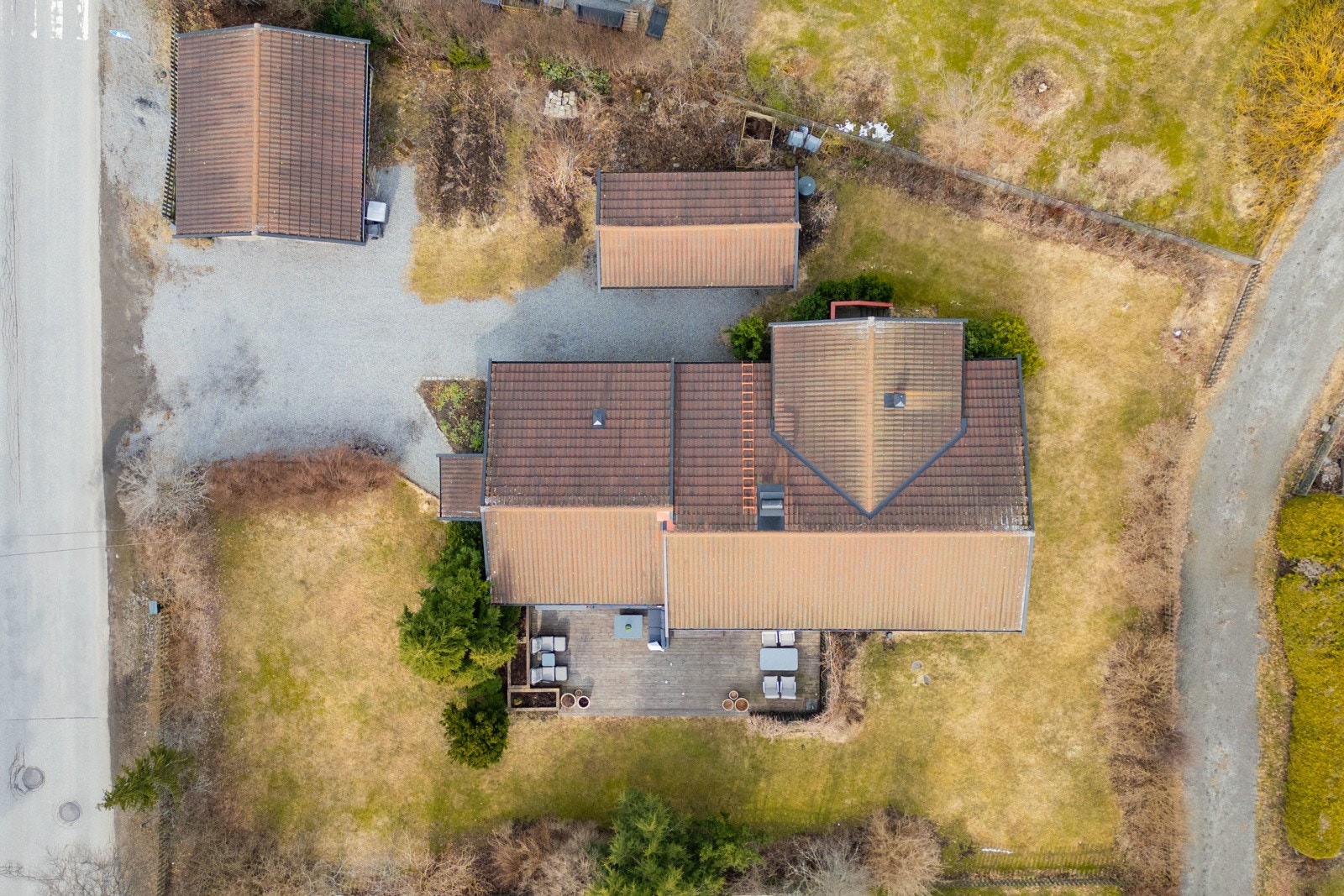 Oversiktsbilde av eiendom med tre bygninger, stor terrasse og gruslagt parkeringsområde. Galleribilde