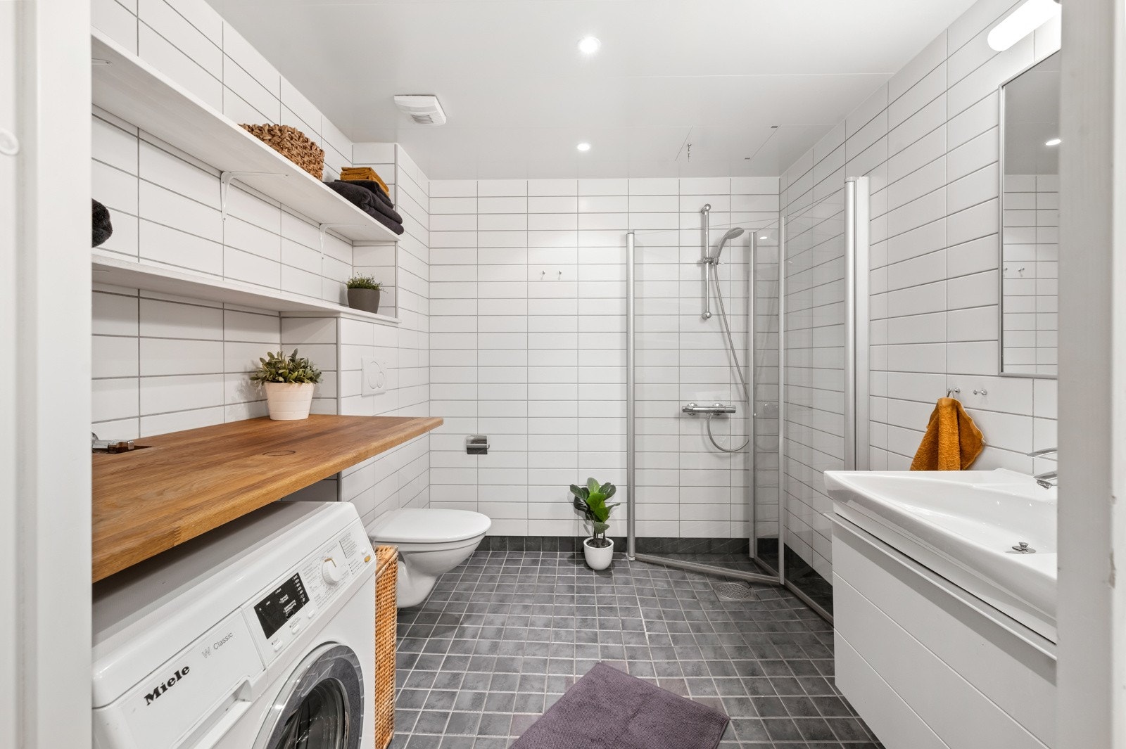 Leiligheten har et stilrent og funksjonelt baderom med flislagte vegger og panelplater i himling Galleribilde