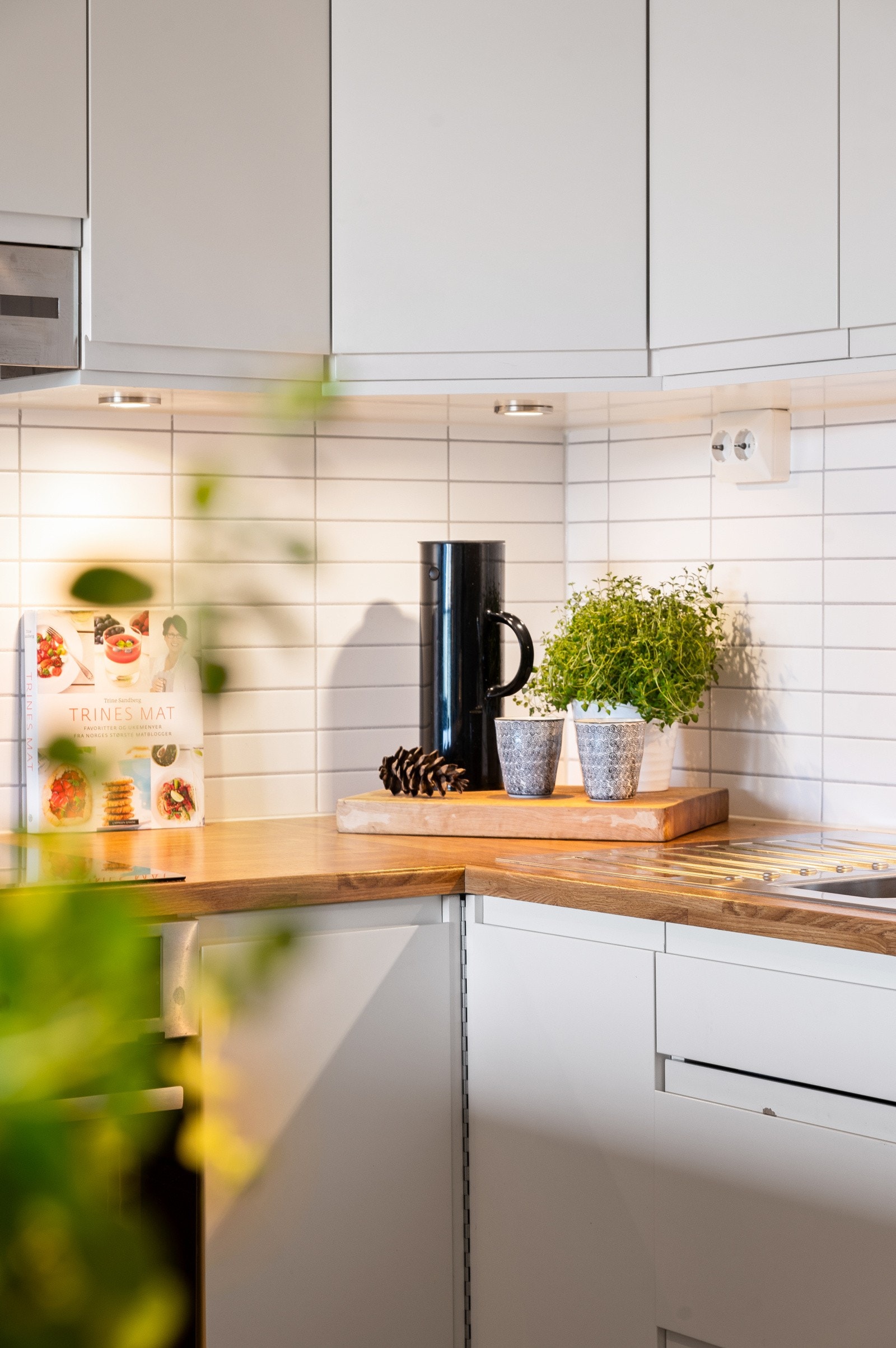 Mellom benk og overskap er det fliser på vegg og belysning under overskap, for et rent og elegant preg Galleribilde