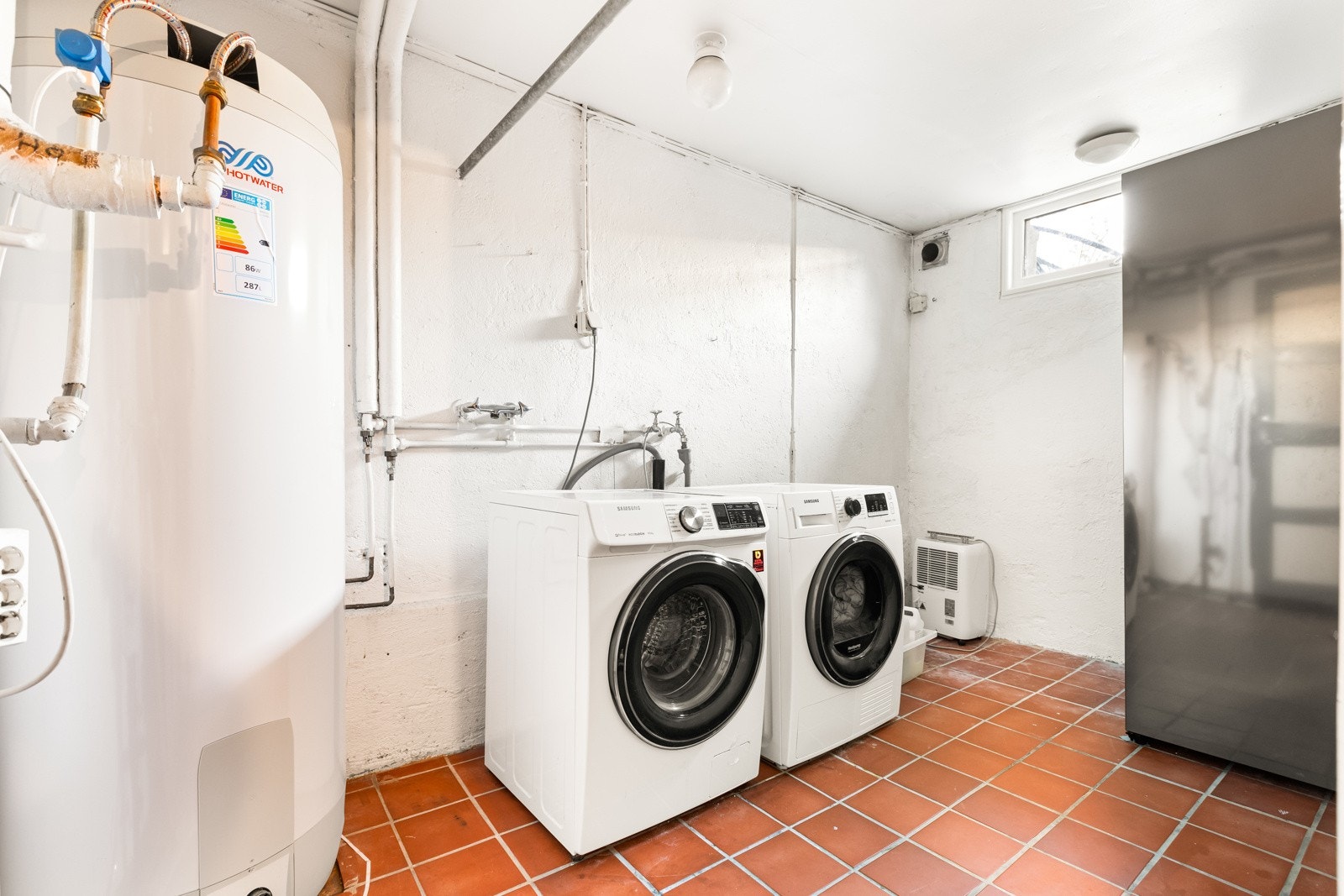 Et stort praktisk vaskerom med opplegg for vaskemaskin og tørketrommel. Varmtvannbereder på 281 liter er plassert på vaskerommet (2021). Berederen er lekkasjesikret med waterguard og sluk. Galleribilde