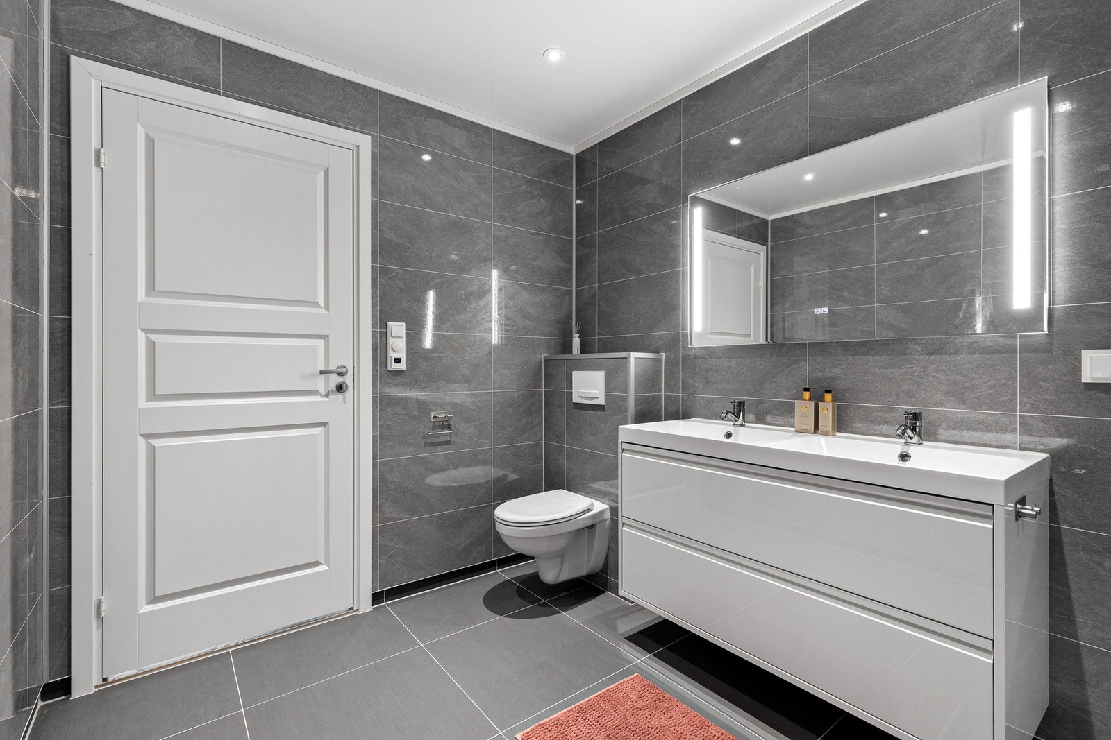 Badet er innredet med vegghengt toalett, servantskap med ovenpåliggende dobbel servant, dusjhjørne og opplegg for vaskemaskin og tørketrommel Galleribilde