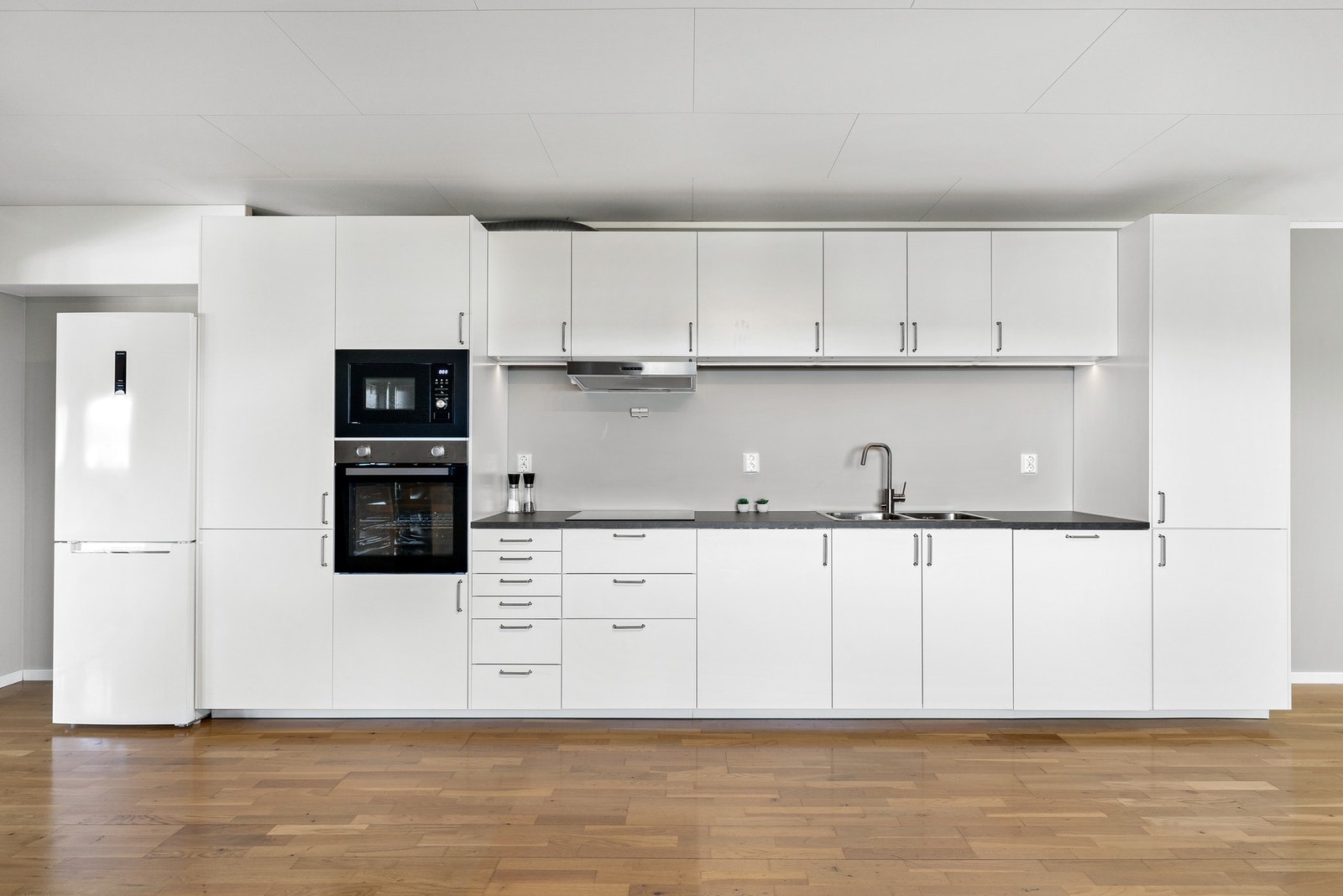 Stilren kjøkkeninnredning fra 2024 med integrerte hvitevarer som komfyr, mikrobølgeovn og oppvaskmaskin Galleribilde