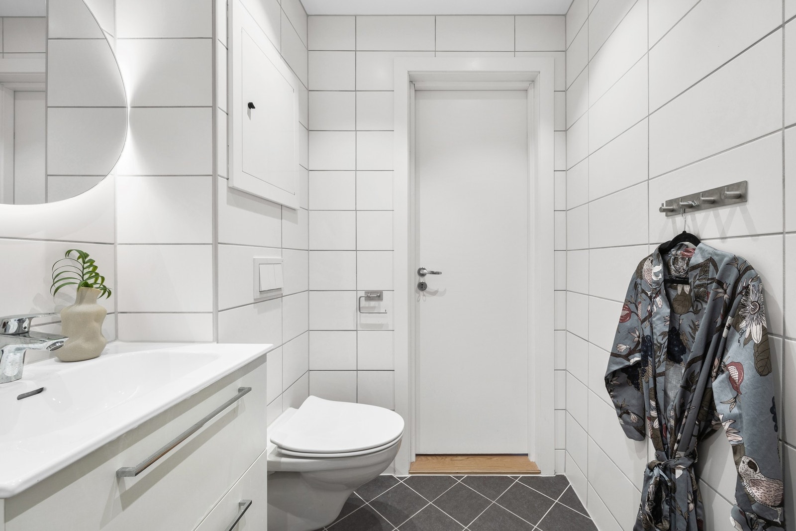 Innredningen er funksjonell og fin med heldekkende servant på hvit skuffeseksjon, rundt speil med rammebelysning. Galleribilde
