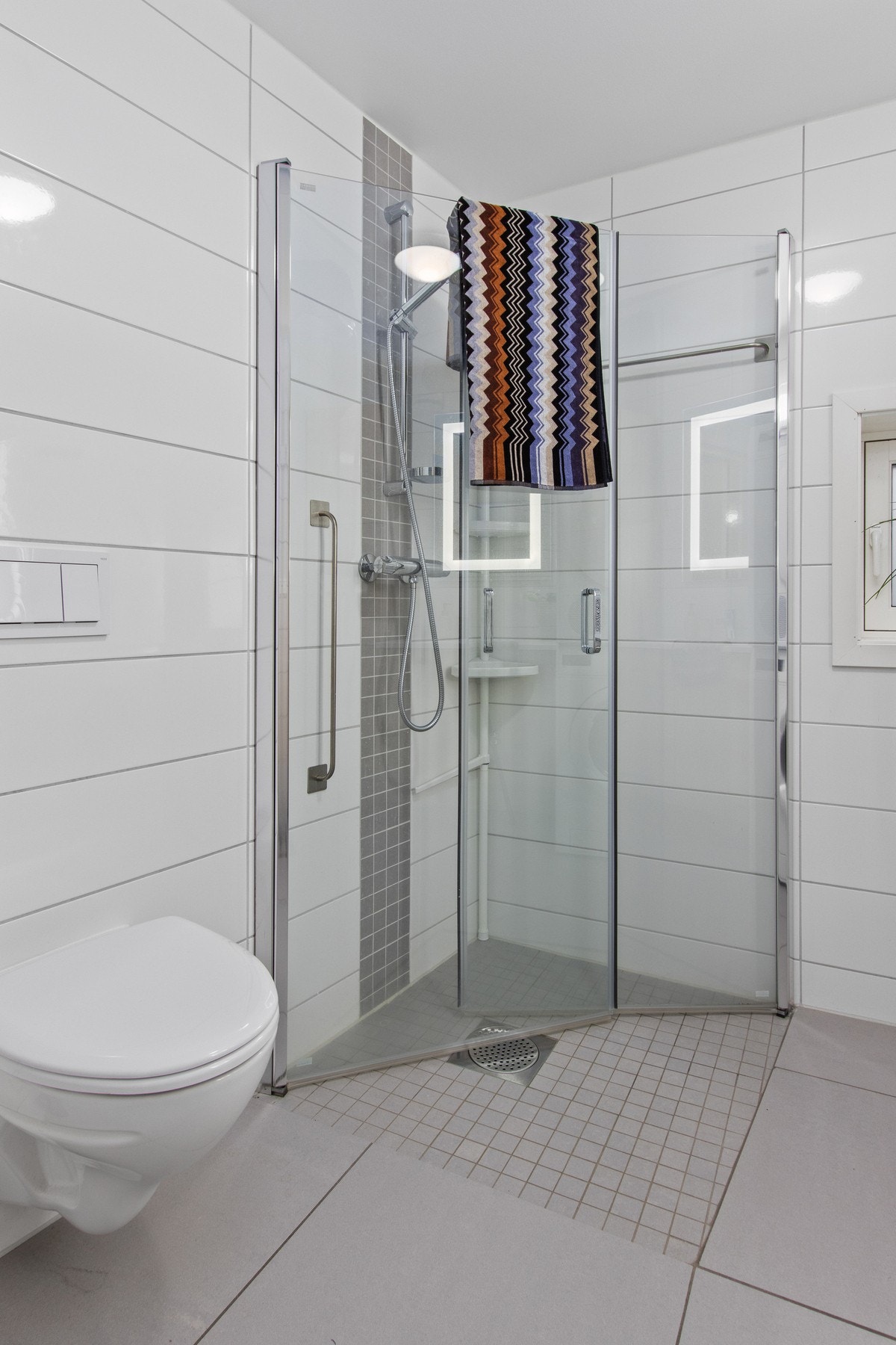 Badet inneholder dusj med glass-dører, vegghengt wc med innebygd sisterne, servant i innredning og opplegg for vaskemaskin og tørketrommel. Galleribilde