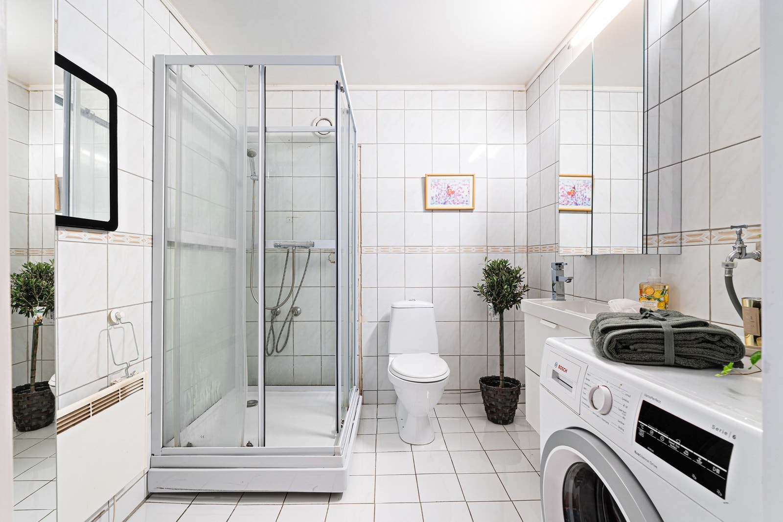 Badet har flis på gulv og vegg, dusjkabinett, servant med underskap, toalett og opplegg for vaskemaskin. Galleribilde