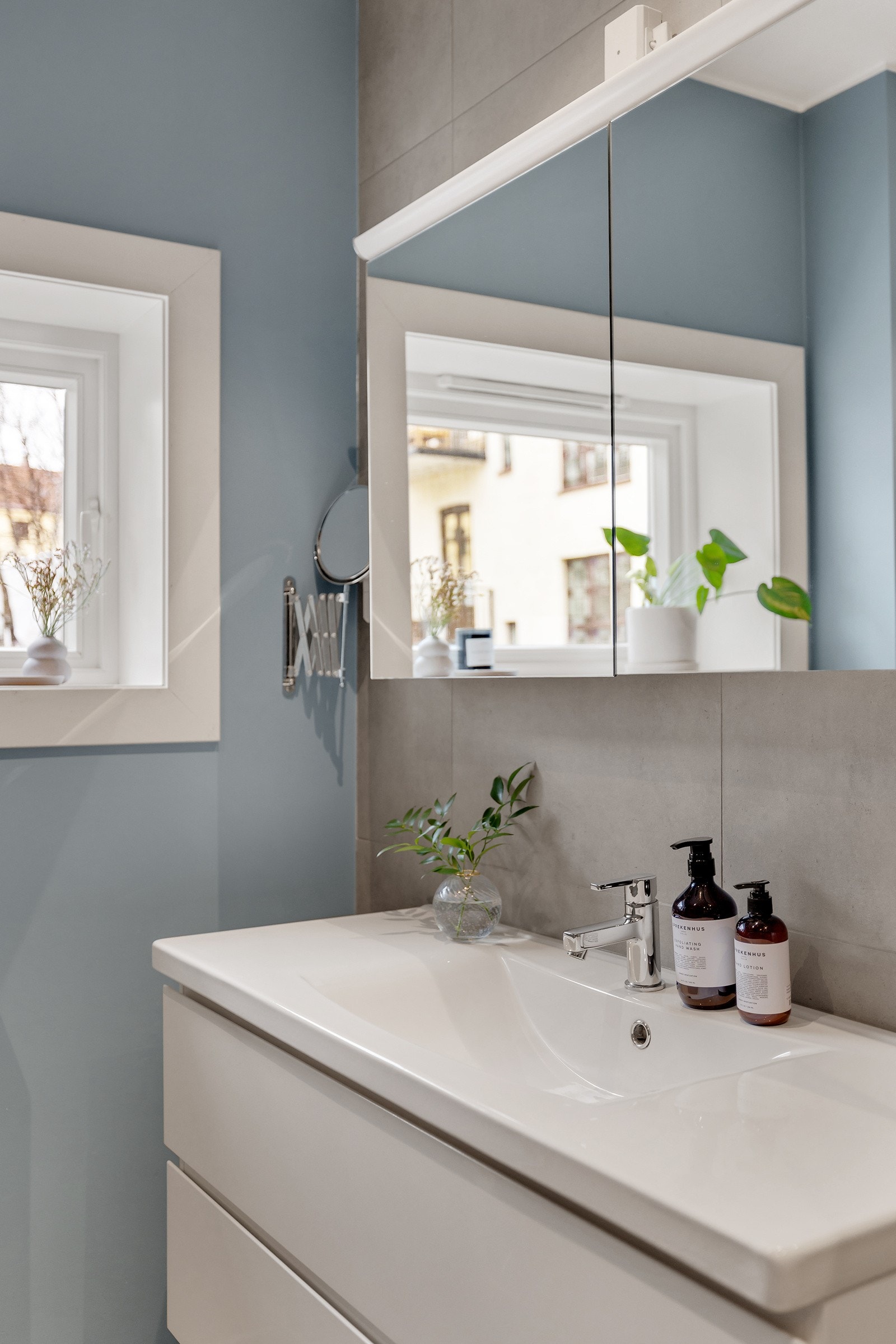 Badet inneholder vegghengt innredning med skuffer og heldekkende servant, stort speilskap, vegghengt wc og dusjhjørne med glassdører. Galleribilde