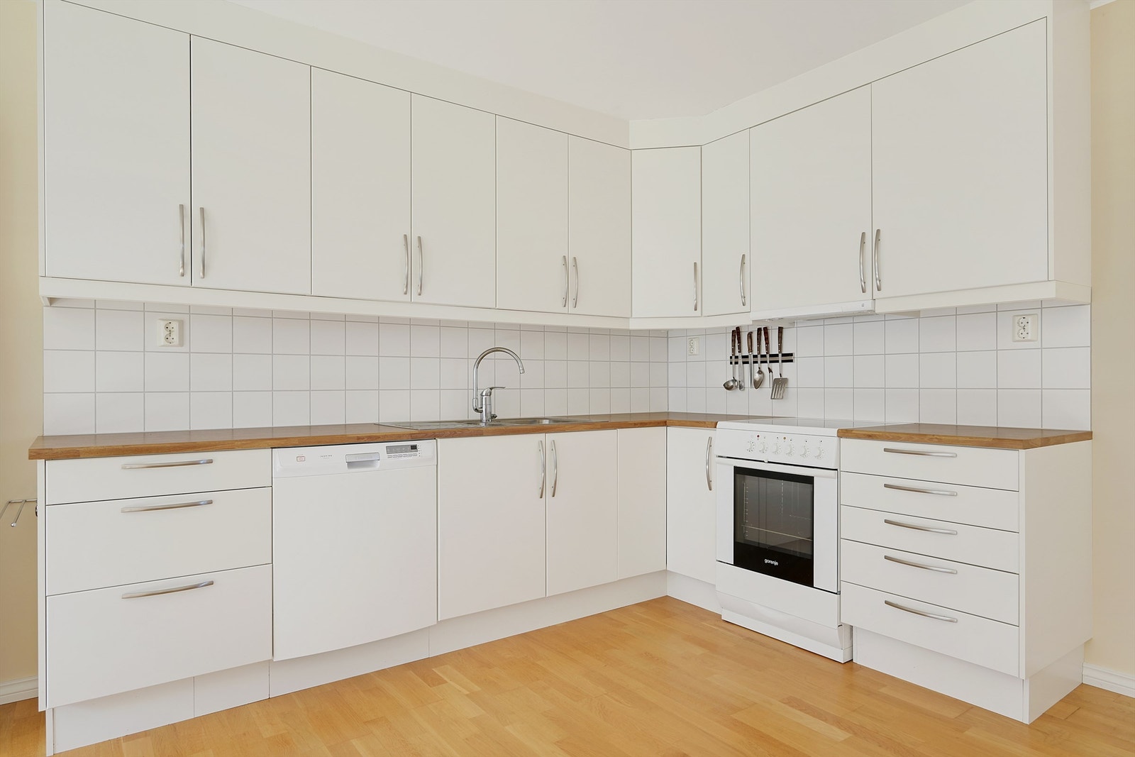 Eier valgte L-løsning på kjøkken med takhøye skap. Fliser over benker. Galleribilde