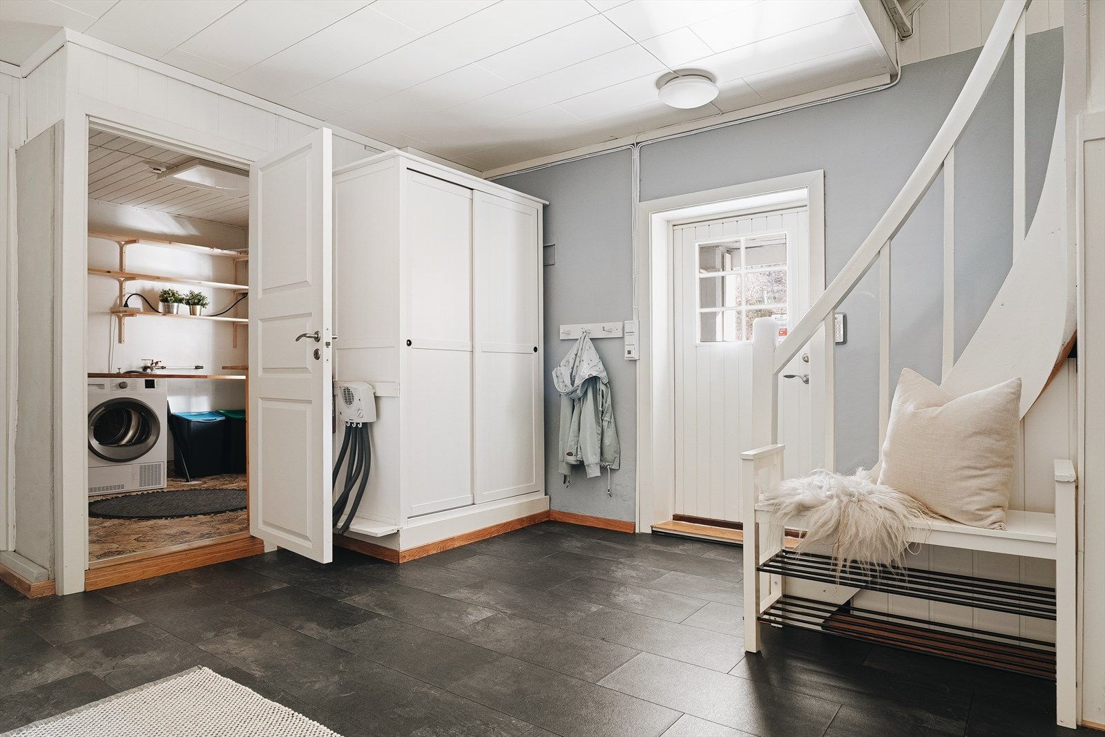 Egen inngang nede hvor entréen er lys og romslig, med laminatgulv og lysmalte vegger. Den har en praktisk garderobeløsning og oppbevaringshyller som gir godt med plass til yttertøy og sko Galleribilde