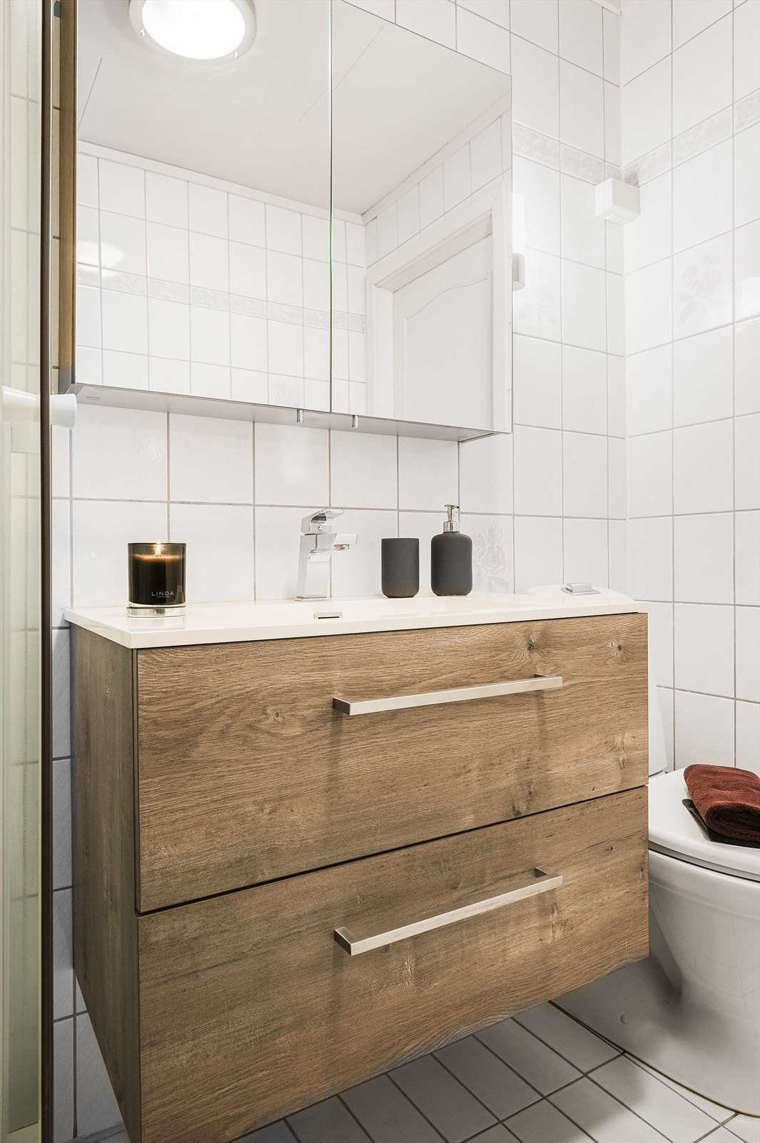 Baderomsinnredning med servant på underskap og speilskap over. Veggmontert langskap for ekstra oppbevaring. Galleribilde