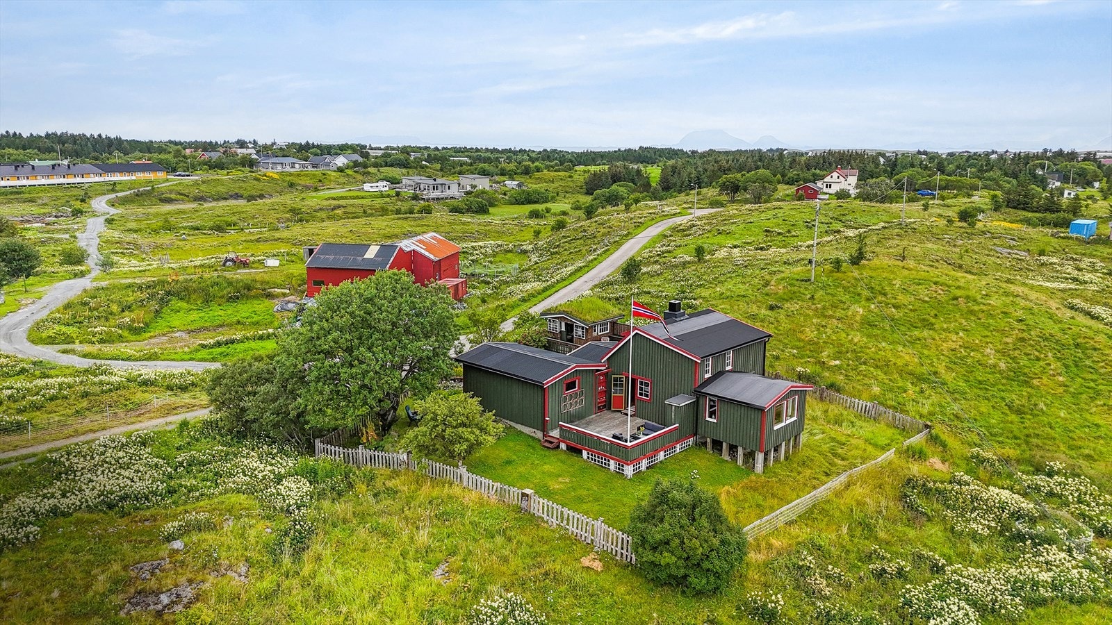 Fritidsboligtomten er opparbeidet med plen, prydbusker, steinbelagt gårdsplass, steinmurer og flere trær - blant annet et spektakulært gammelt tre på tomten lengst vest. Galleribilde