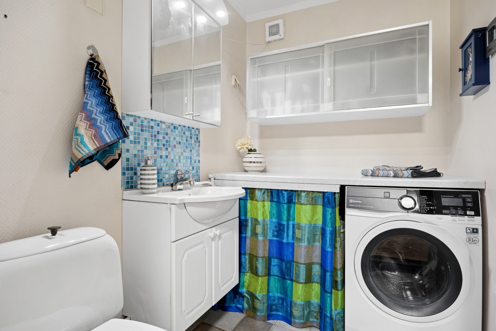 Vaskerommet har flislagt gulv og er utstyrt med toalett, servant og flere skap til oppbevaring. Galleribilde