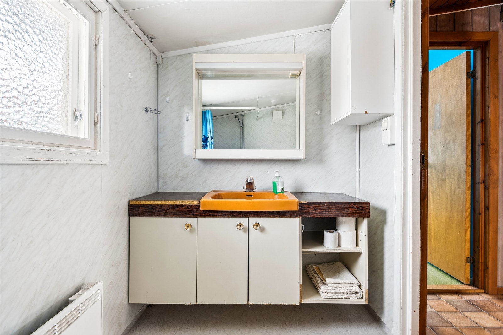 Badet ligger i tilbygget fra 1976 med belegg på gulv, baderomsplater på vegger malte plater i himling. Innredet med servantskap med glatte fronter (det er skader på benkeplate og svellskader på dør) og speil med defekt lys. Galleribilde