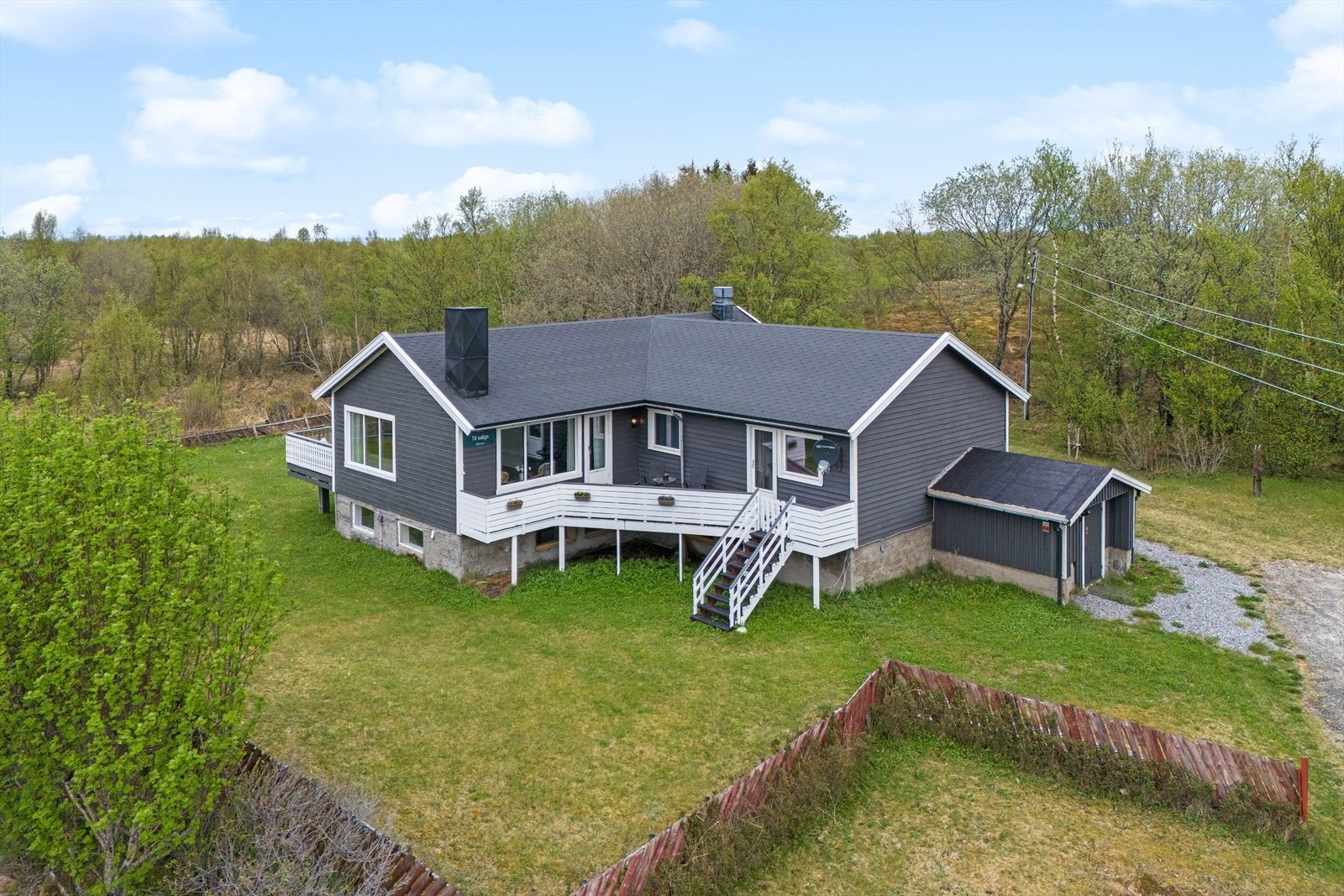 Fra verandaen er ned trapp ned til en flott hage med tilnærmet flatt gressplen og noe beplantning Galleribilde