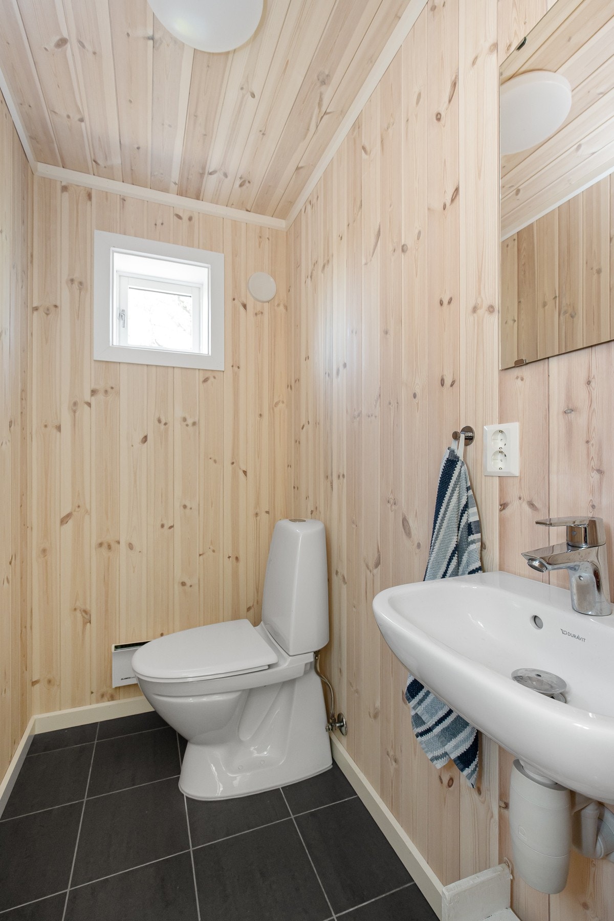 Lyst og praktisk toalettrom med flislagt gulv og heltre panel på vegger og tak. Galleribilde