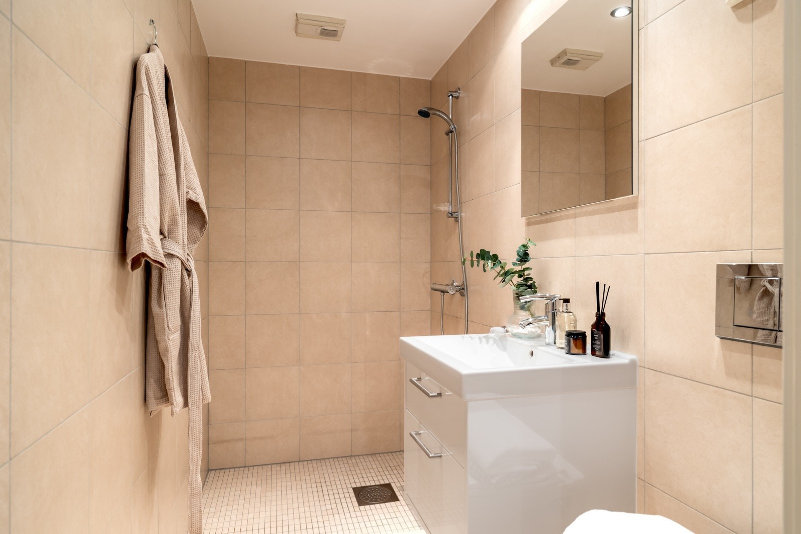 Den hvite skuffeseksjonen har heldekkende servant, og over er det et stort speil. I tillegg til et vegghengt toalett har badet åpen dusjløsning. Galleribilde