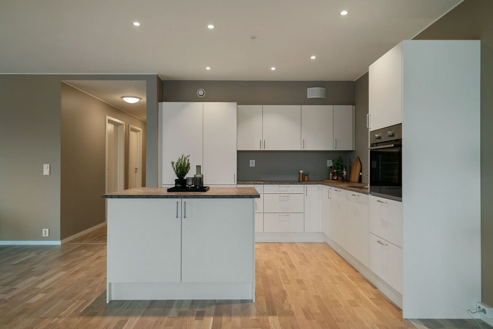 Stilrent kjøkken med integrerte hvitevarer og kjøkkenøy. Stekeovnen er plassert i god arbeidshøyde. Galleribilde