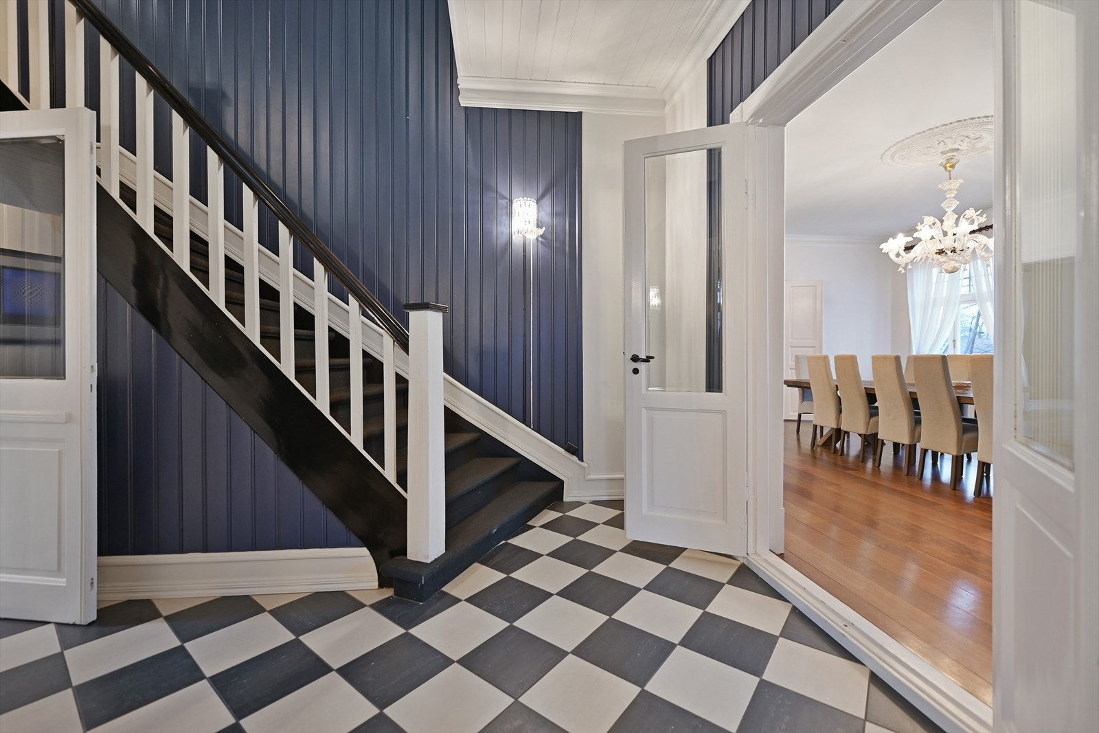 Hallen har flislagt gulv i sjakkmønster med varmekabler og trapp opp til boligens 2. etasje. Galleribilde