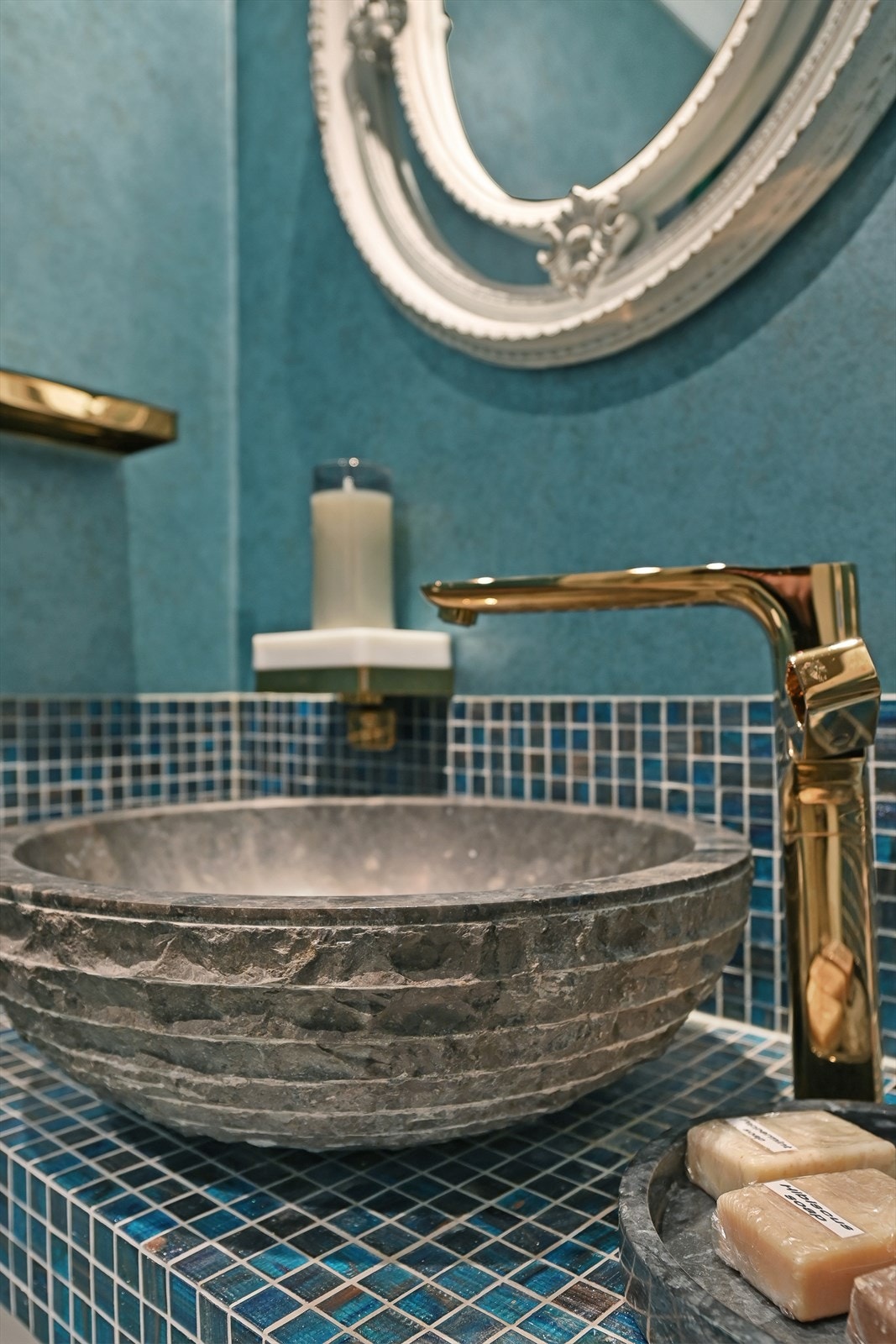 Rommet har mosaikkflislagt benk med frittstående rund steinvask og gullfarget servant. Galleribilde