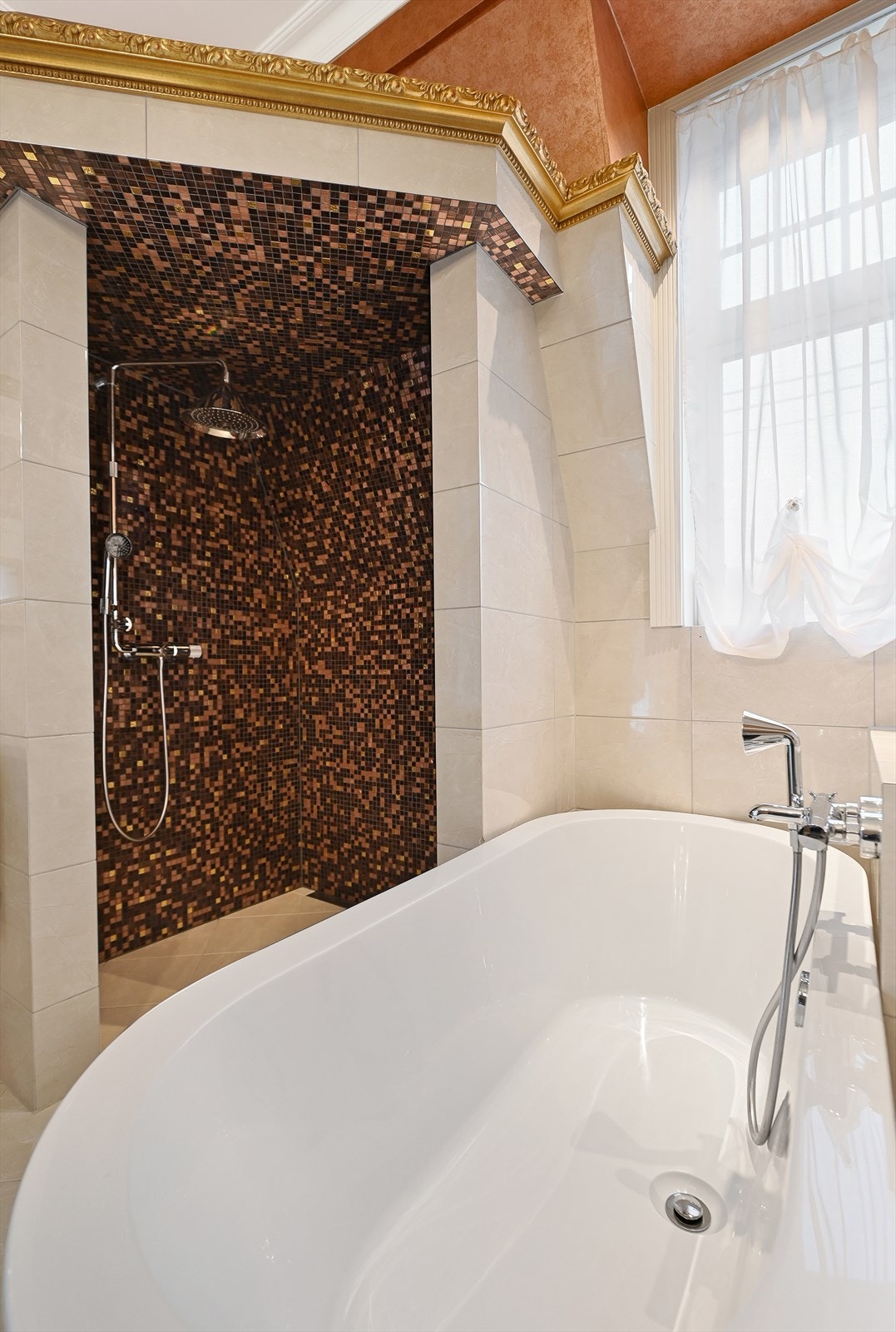 Det er gulvvarme og en dekorativ dusjnisje med mosaikkflis, lys og regnfallsdusj, samt badekar. Galleribilde