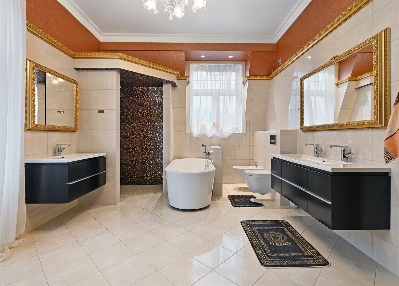 Badet har et elegant uttrykk med store, flislagte overflater og gulldetaljer, samt utgang til sydvendt veranda. Galleribilde