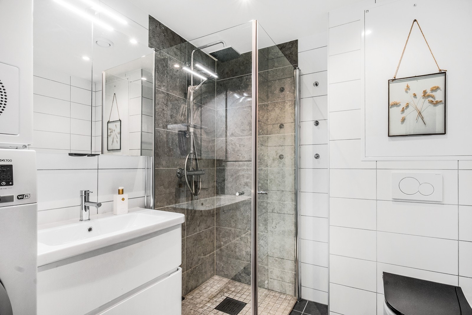 Boligens bad fremstår lyst og tidløst, med flislagte overflater, gulvvarme og downlights. Galleribilde
