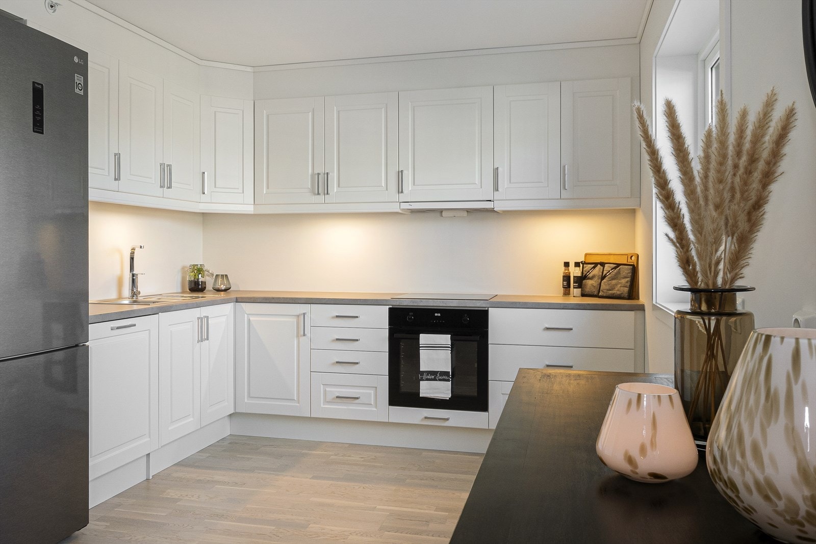 Lyst og klassisk kjøkken i åpen løsning til stuen med sømløs overgang mellom tak og overskap. Galleribilde