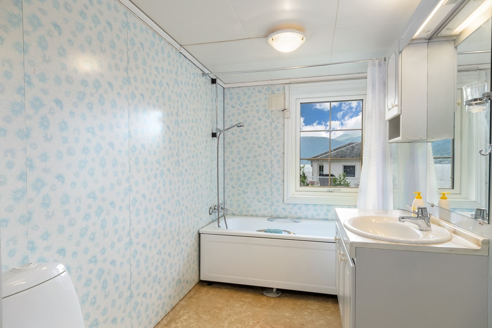 Badet har baderomsplater på veggar og belegg på golv. Badet er utstyrt med nedfelt servant med underskåp og overskåp, badekar med enkel dusj og toalett. Galleribilde