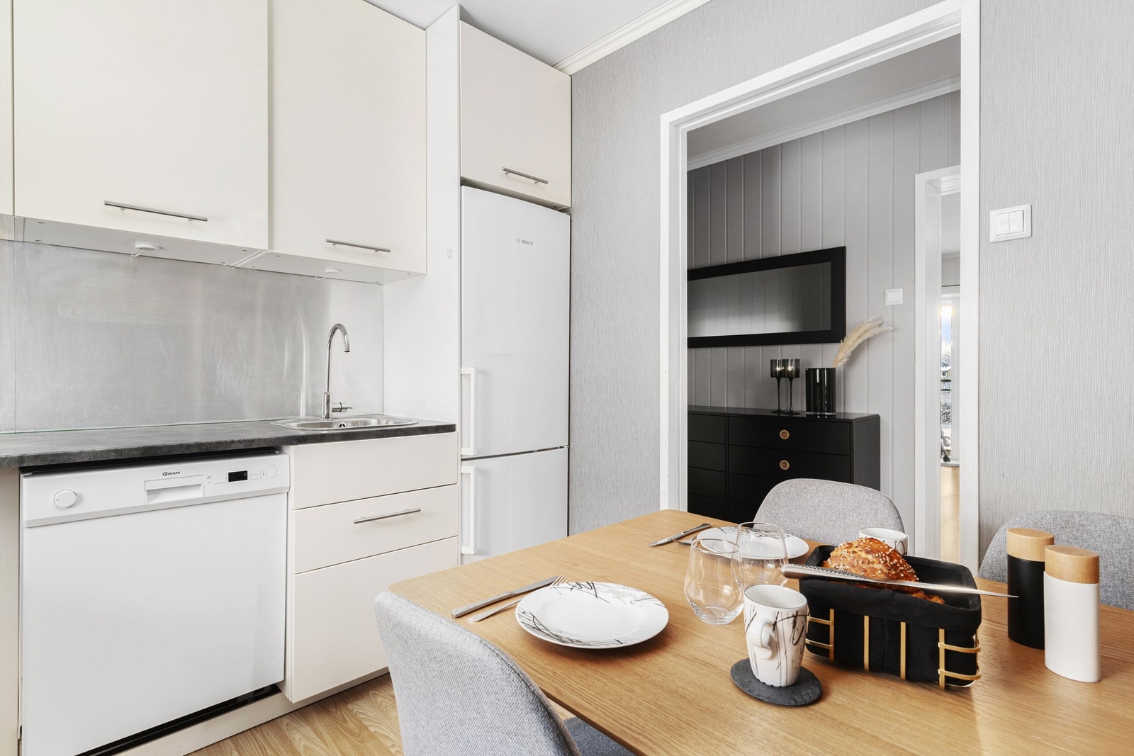 Videre er innredningen utstyrt med integrert stekeovn og platetopp, sort vegghengt ventilator. Frittstående oppvaskmaskin og kjøleskap med frysedel. Alle hvitevarer medfølger salget Galleribilde