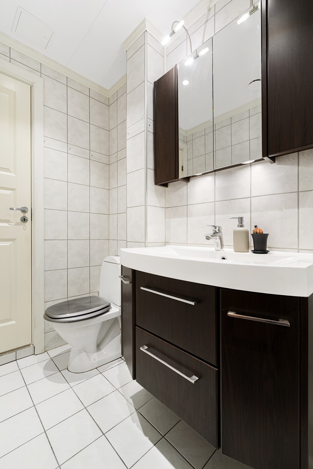 Badet er oppmålt til 4m² med vegghengt baderomsinnredning, med oppbevaringsplass og ovenpåliggende servant, sammen med vegghengt speilskap med stikkontakt og downlights i underkant.
Dusjkabinett i hjørne, opplegg for vaskemaskin i tillegg til ny varmtvann Galleribilde