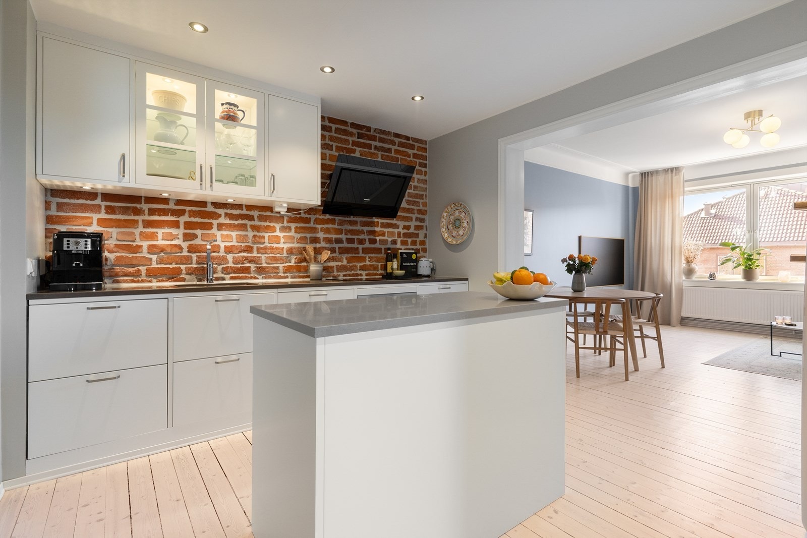 Stilrent og innbydende kjøkken med rustikk mursteinsvegg som skaper karakter. Den åpne planløsningen mot stue og spiseplass gir en sosial og luftig atmosfære, perfekt for både hverdag og gjester. Galleribilde