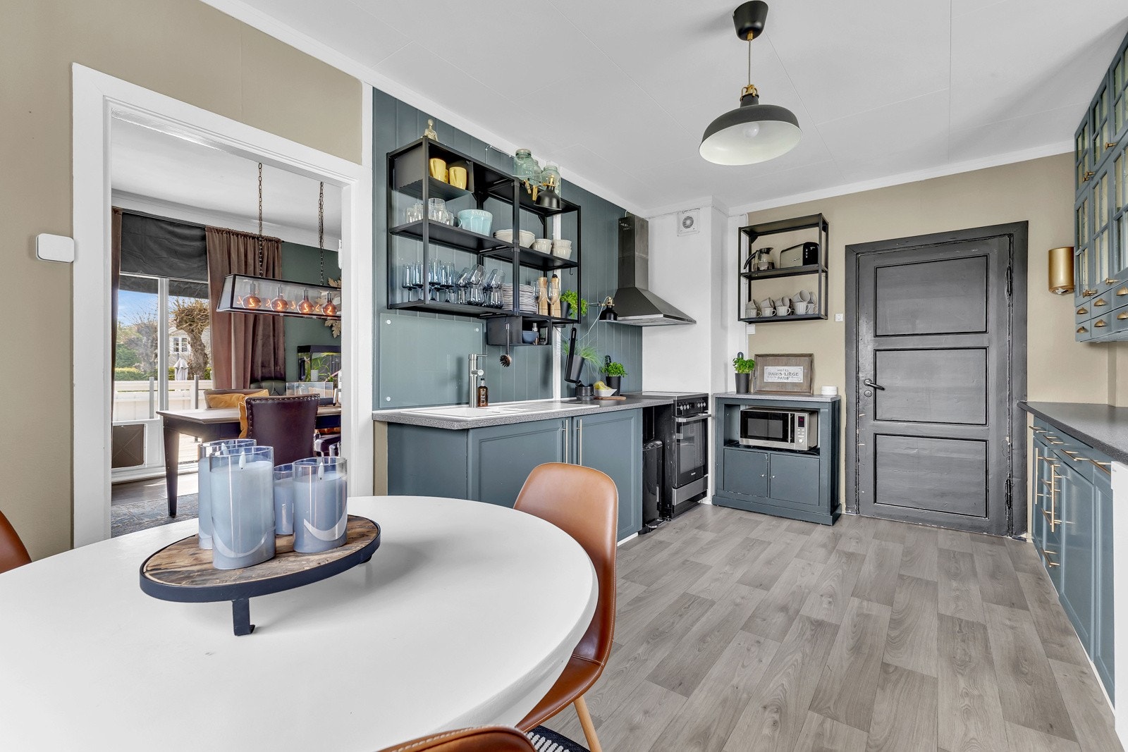 Innredningen har blågrønne, profilerte fronter, messingdetaljer, vitrinedører og grå laminatbenkeplate med nedfelt kum i hvit kompositt. Galleribilde