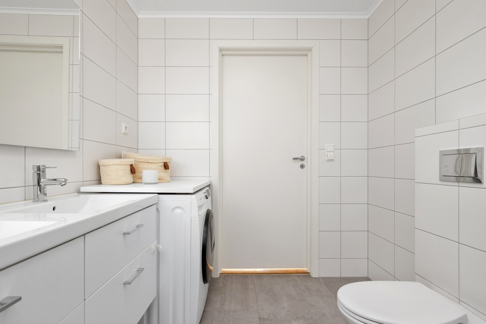 Badet har pene overflater - gråbeige fliser på gulvet og endeveggen, hvite fliser på øvrige vegger, gulvvarme og dagslys fra et lite vindu i endeveggen. Galleribilde