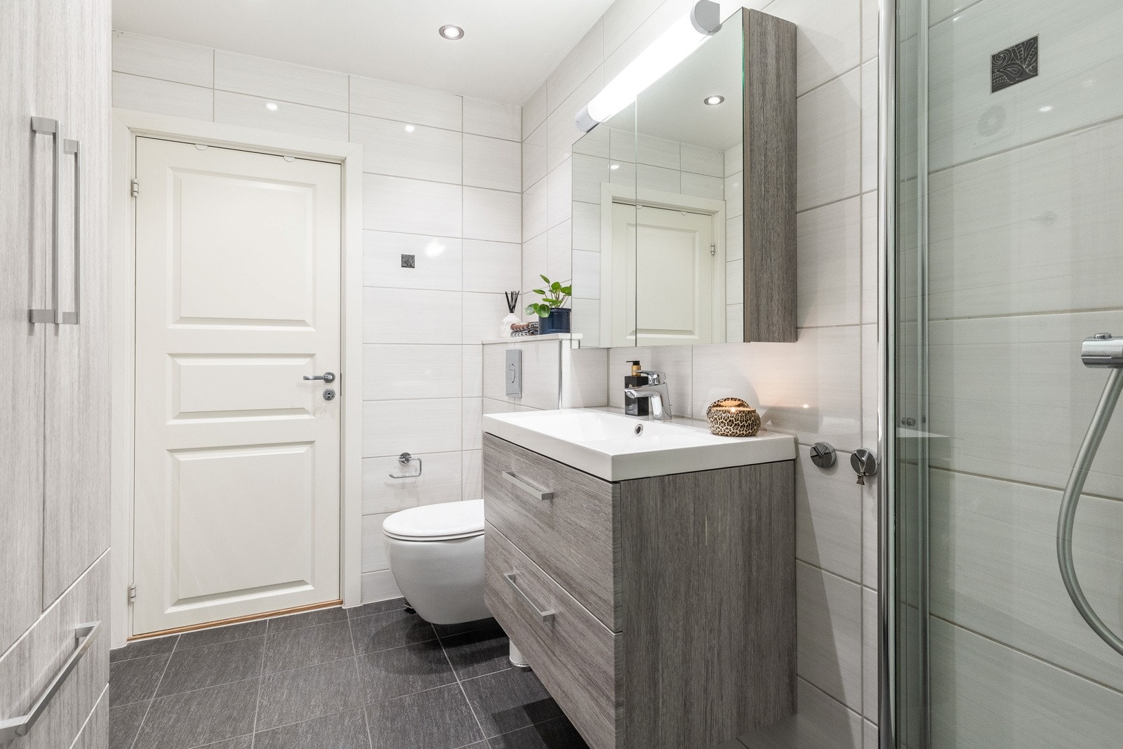 Baderommet inneholder: servant med speilskap og belysning, dusjhjørne og veggmontert wc. Ytterligere fastmontert skap for ekstra oppbevaring. Galleribilde