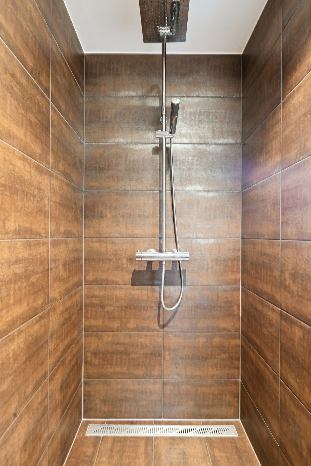 Romslig dusjhjørne med stilige fliser i kobberlook og en herlig regndusj. Perfekt for en spa-lignende opplevelse hjemme. Galleribilde