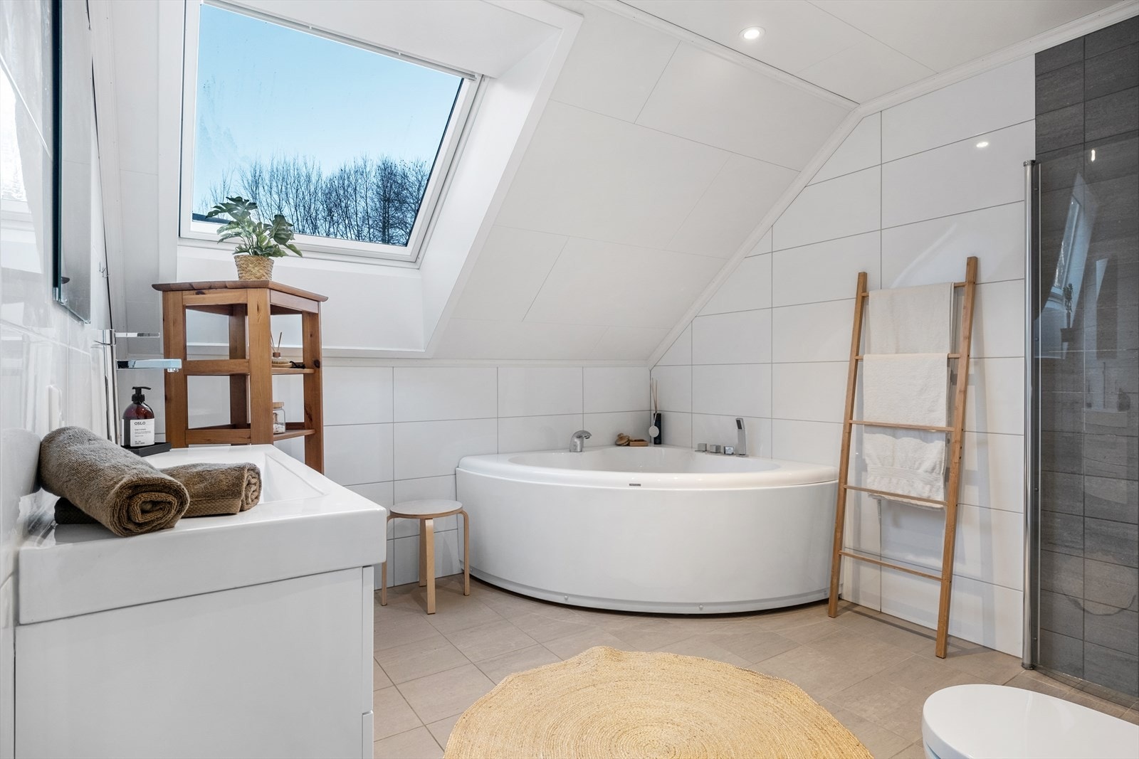 Badet er innreia med vegghengd toalett, servant med underskåp, hjørnebadekar og dusjhjørne med innfellbare dører. Galleribilde