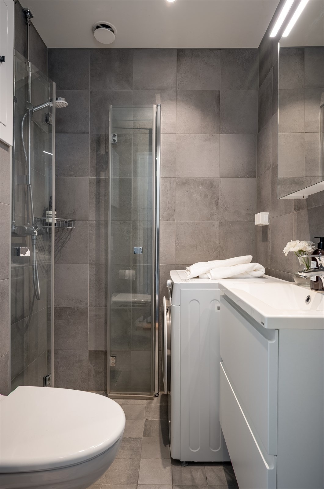 Innredet med servant med skuffer, speilskap med belysning, veggmontert klosett, dusjvegger og opplegg for vaskemaskin. Galleribilde