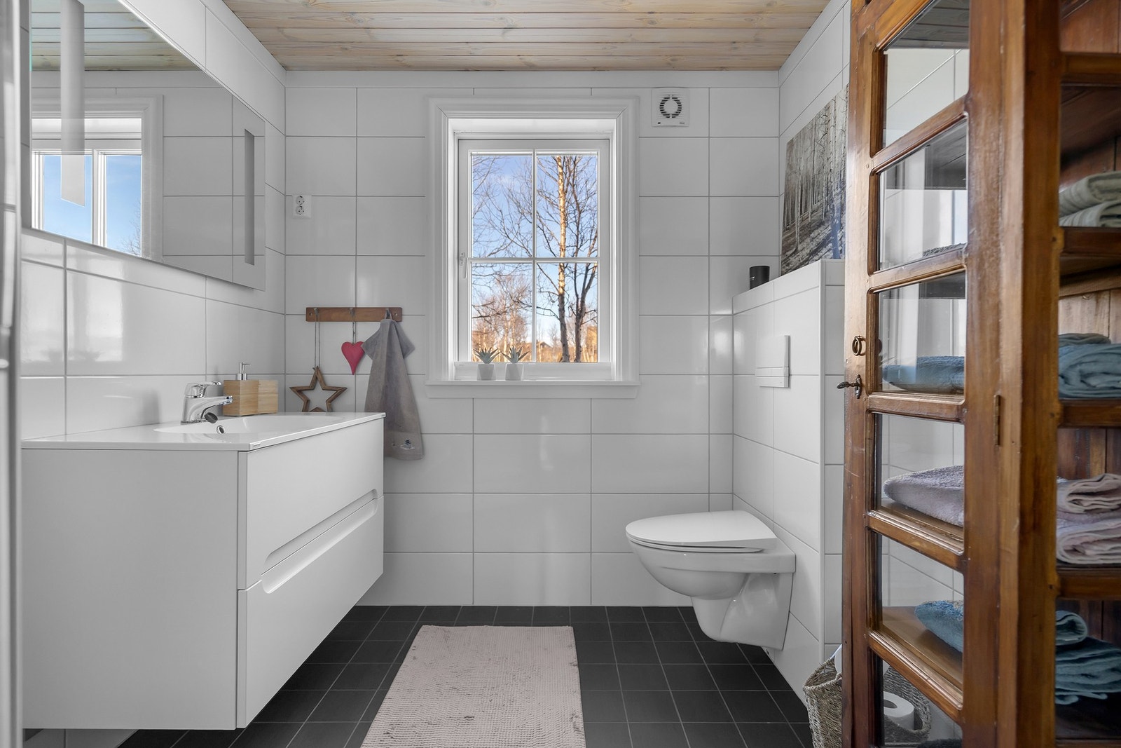 Fra badet i første etasje - vegghengt toalett, baderomsinnredning med porselenstopp, speil med lys og videre er det dusjkabinett Galleribilde