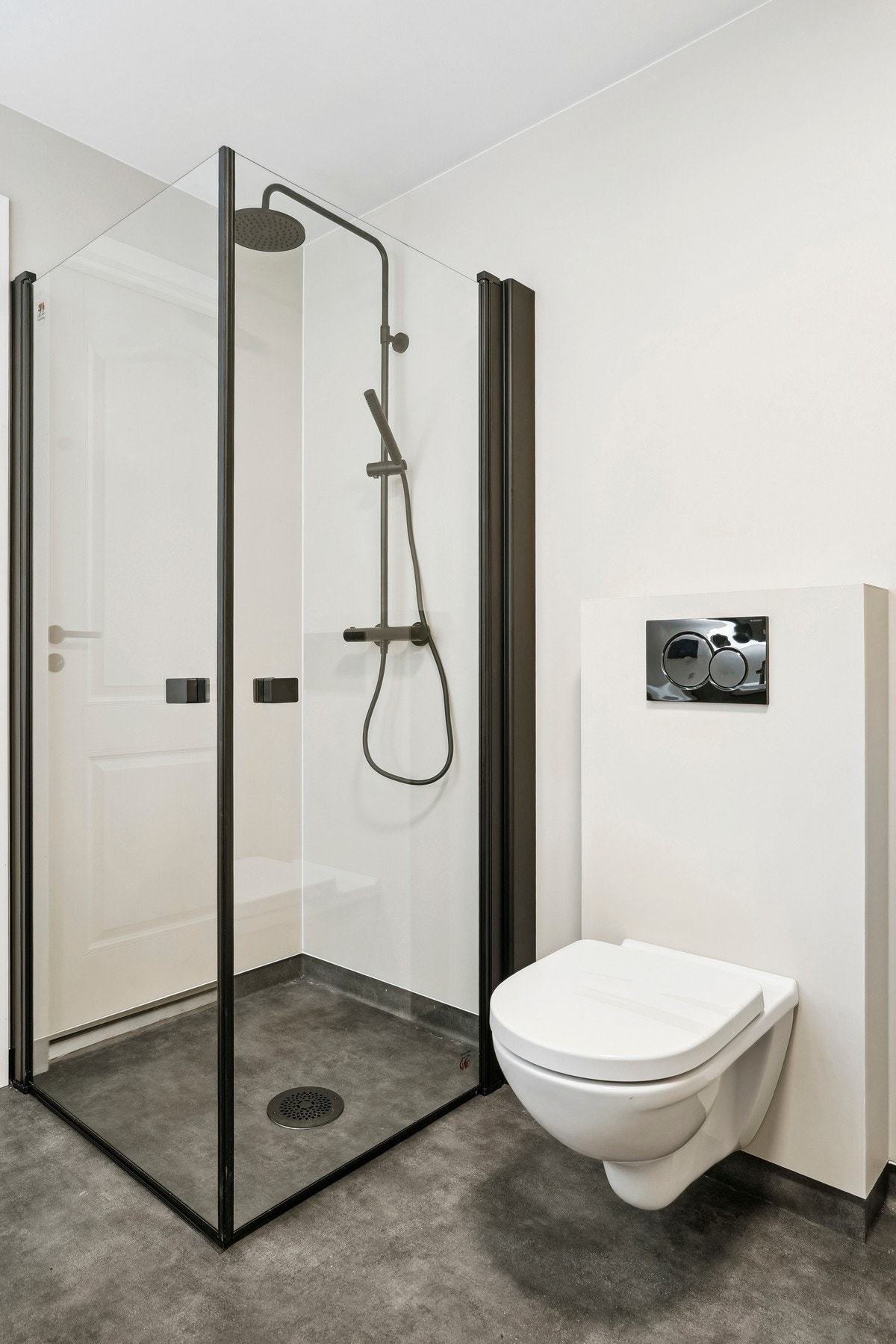 Badet er utstyrt med vegghengt toalett, og dusjhjørne med glassdører og sorte detaljer. Opplegg for badekar. Galleribilde