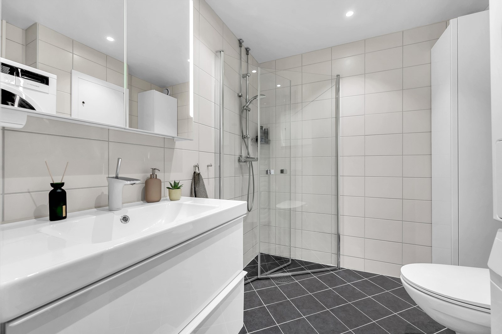 Badet er innredet med vegghengt toalett, servant nedfelt i innredning og dusjhjørne med svingbare glassdører. Det er opplegg for vaskemaskin. Galleribilde