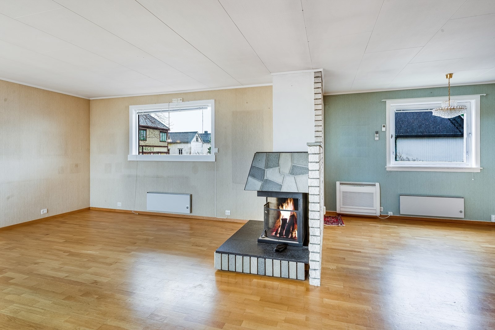 Midt i rommet står en peis som fungerer som et naturlig skille mellom stue og spisestue - kombinert ildsted for fast og flytende brensel. Galleribilde