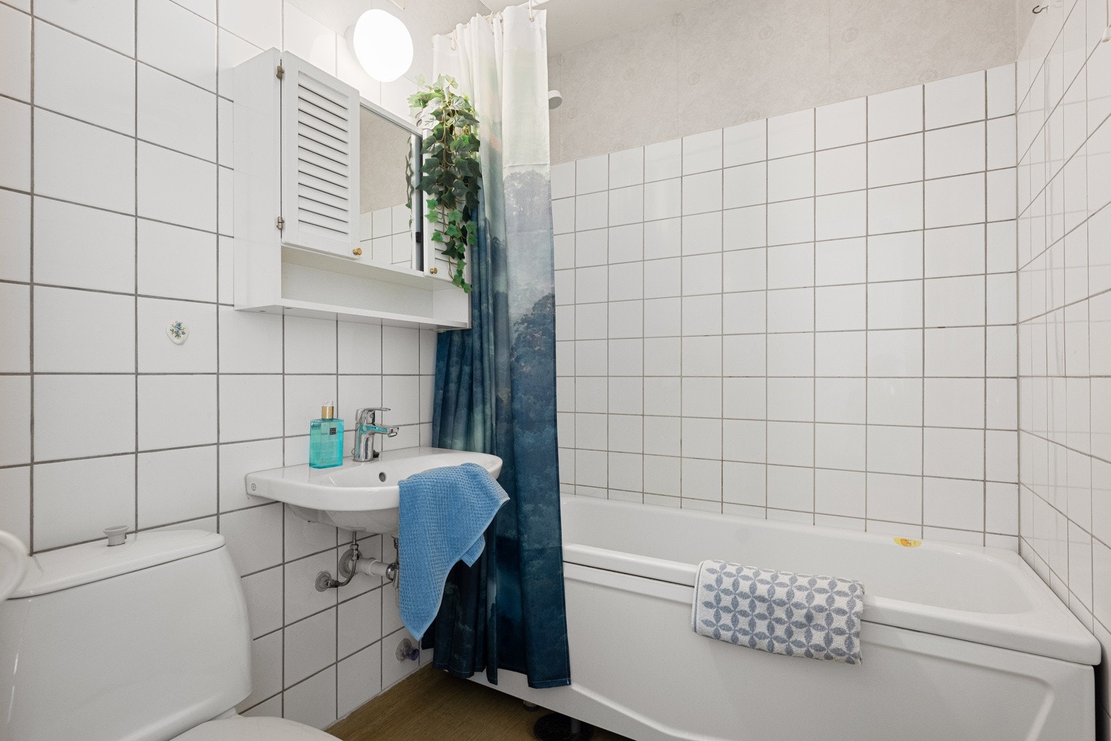 Et lyst bad med toalett, servant, veggmontert speilskap med lys over servant og badekar. Galleribilde