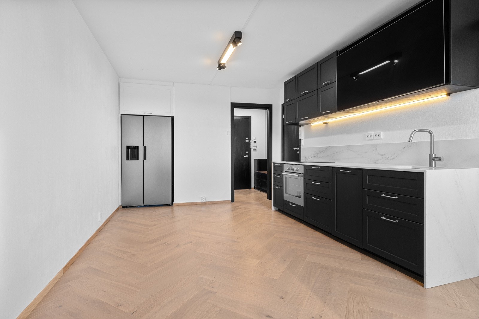 Kjøkkenet fra 2023 inneholder profilerte fronter i sort utførelse og benkeplate av kompositt med underlimt oppvaskkum. Galleribilde