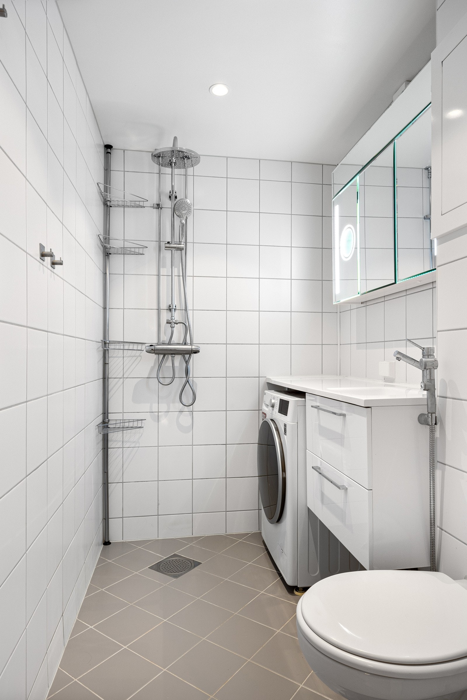 Badet inneholder servantinnredning med skuffer og heldekkende servant, speilskap, vegghengt toalett og dusjhjørne med regnfallsdusj. Galleribilde