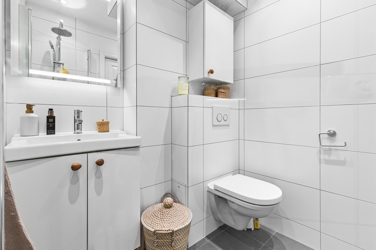 Badet er innredet med servant med underskap, speil med belysning, vegghengt toalett og dusjhjørne med innfellbare glassdører. Galleribilde