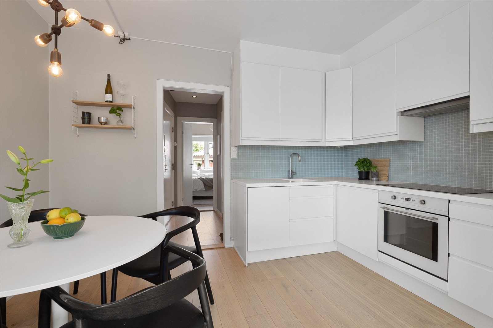 Moderne og stilsikkert kjøkken i åpen løsning. Kjøkkenet er fra 2010 med glatte hvite fronter, dekorative glassmosaikkfliser over benk og akryl benkeplate. Galleribilde